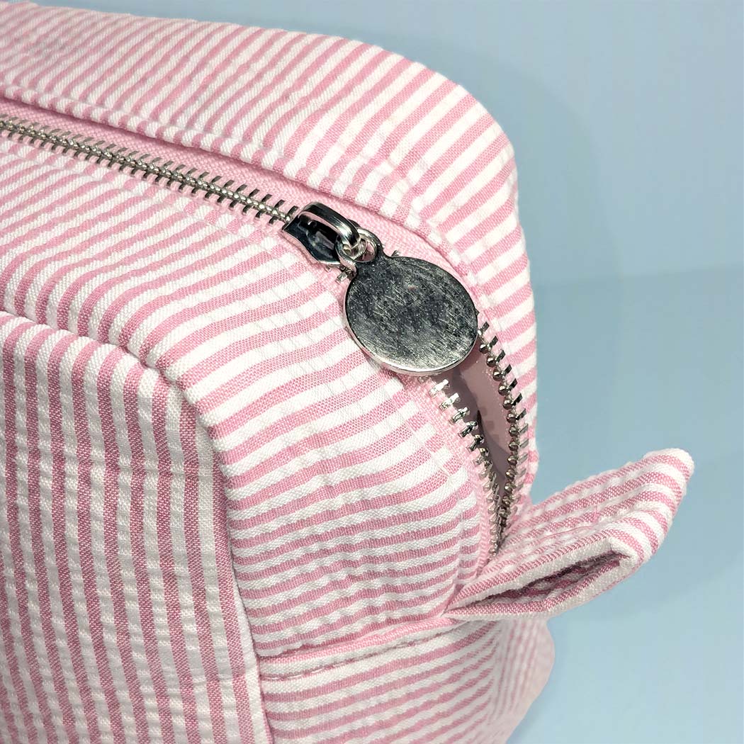 Close-up of a pink and white striped bag with a metal zipper on a light blue background