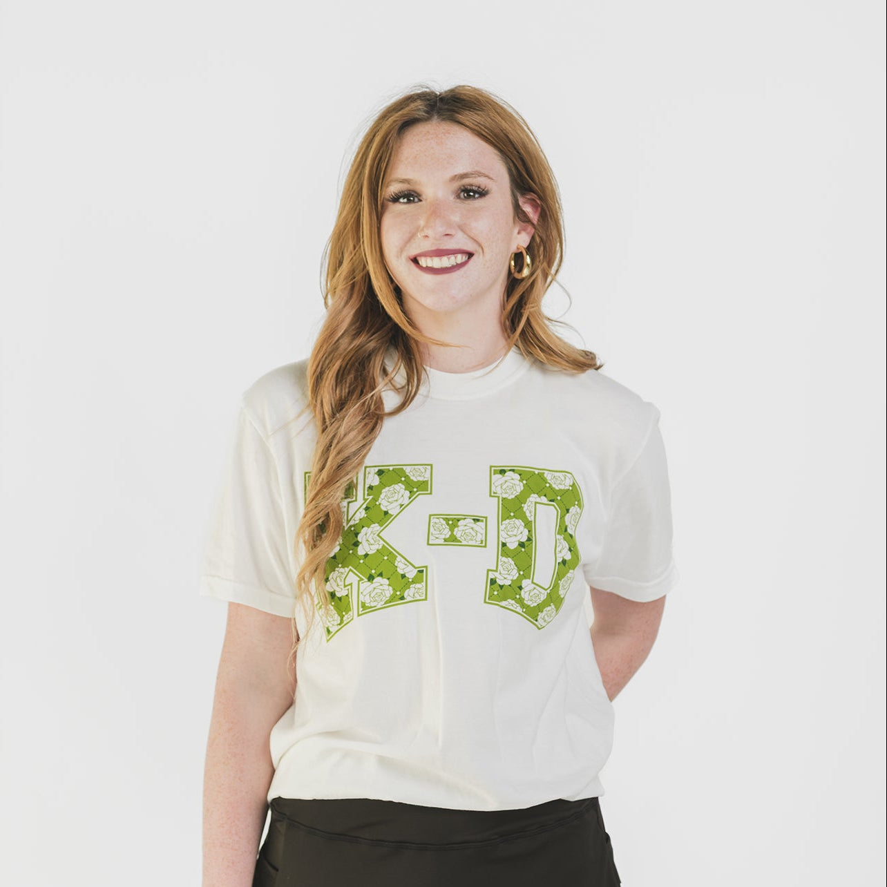 Woman wearing a white t-shirt with green graphics and a black skirt on a white background