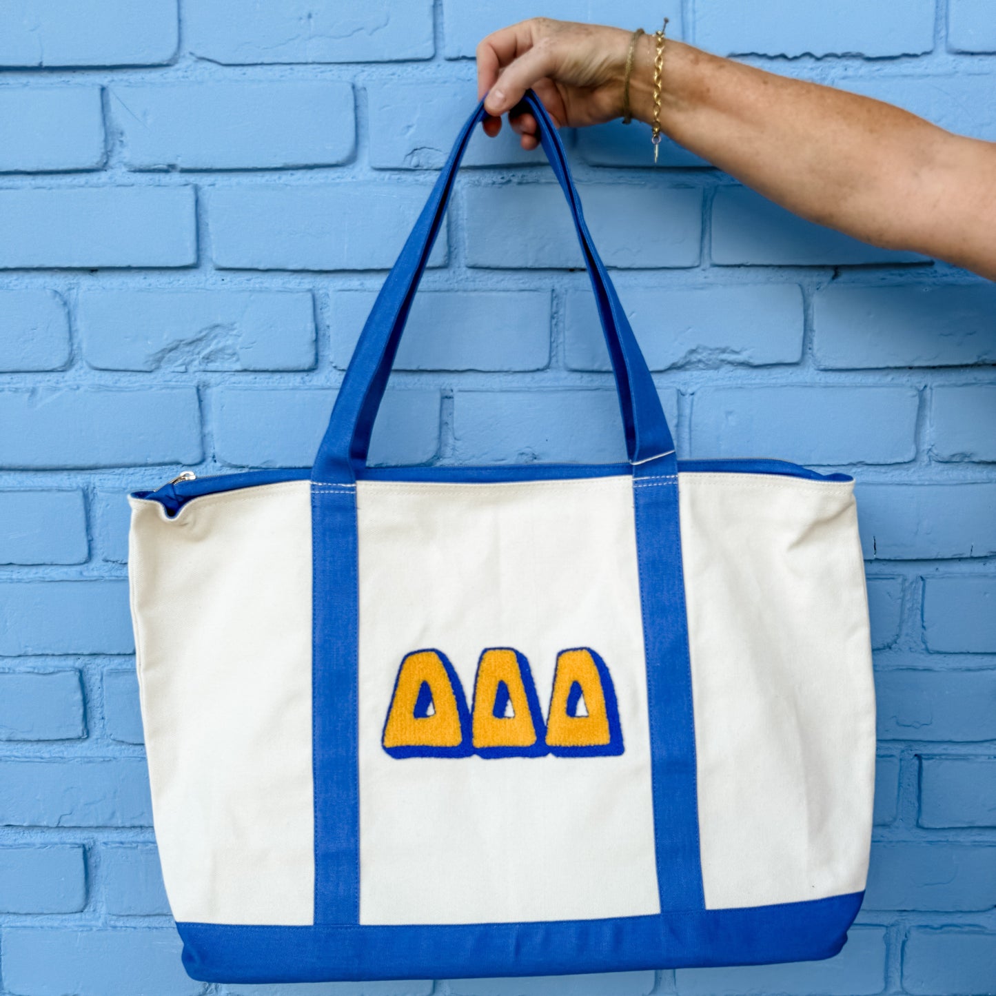 White tote bag with blue handles and yellow symbols against a blue brick wall