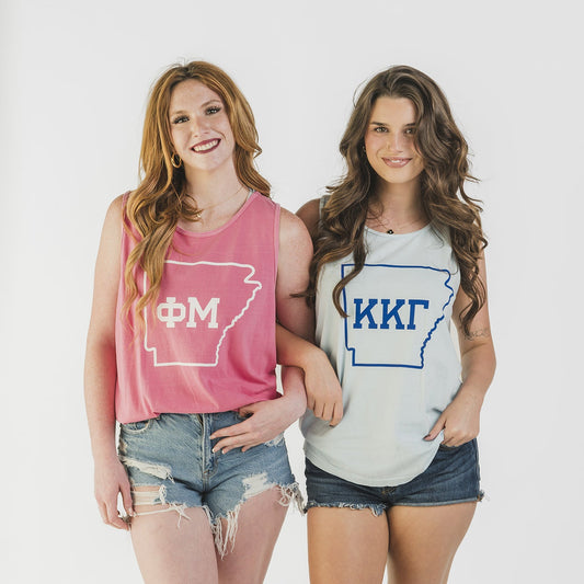 Two women wearing tank tops with Greek letters on a white background