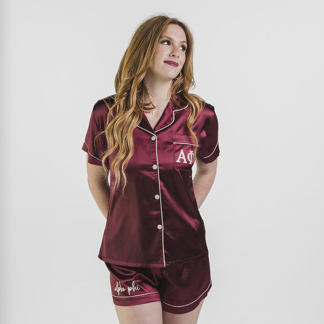 Woman wearing a maroon satin pajama set with white buttons on a plain background